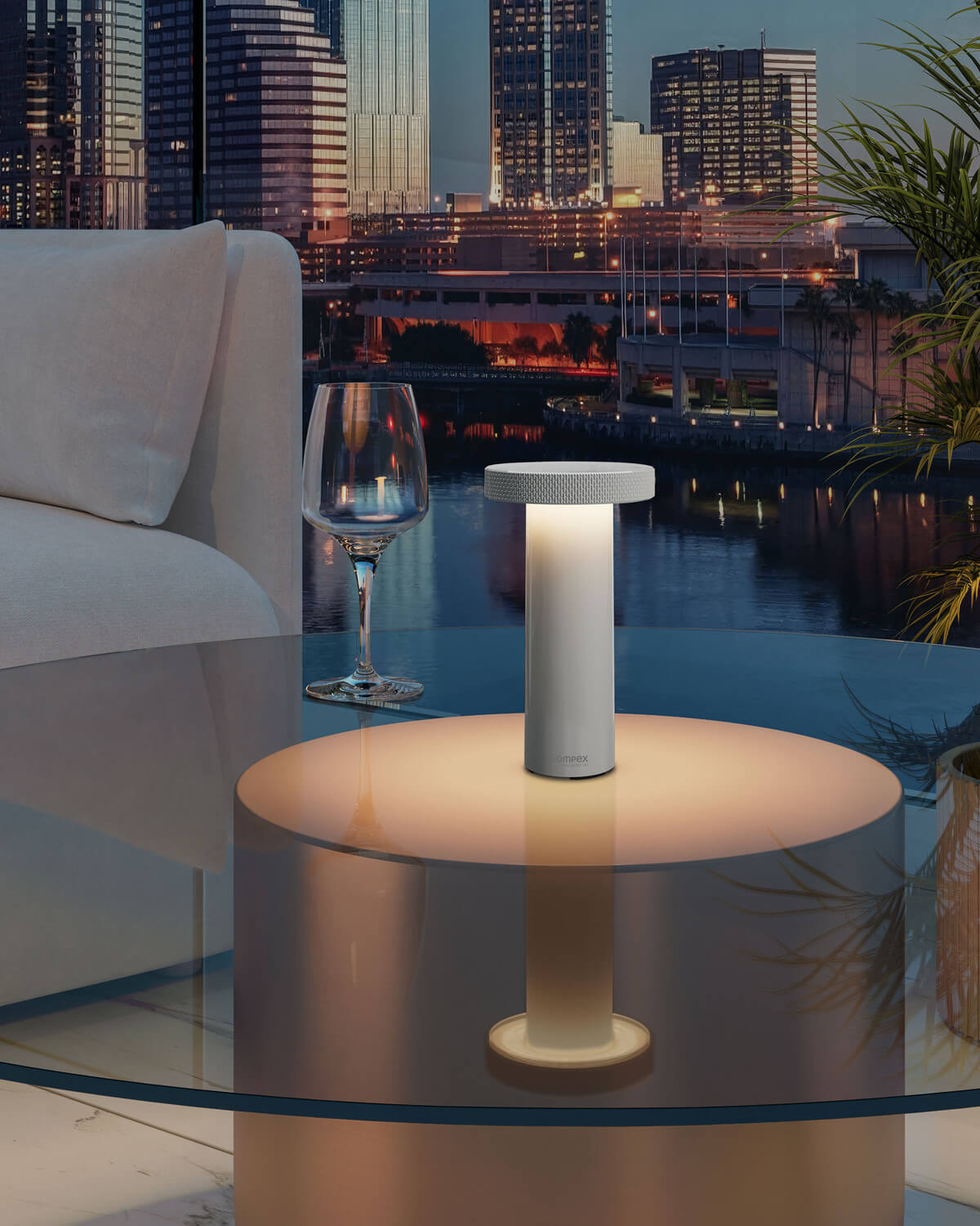 Mise en ambiance nocturne sur table basse en verre, skyline urbaine et verre de vin.
