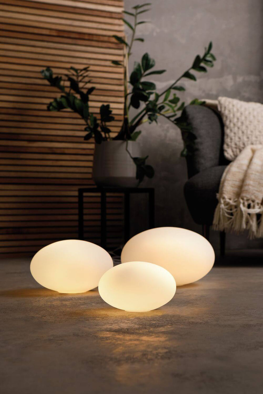 Trois lampes ovales allumées posées au sol dans un intérieur moderne
