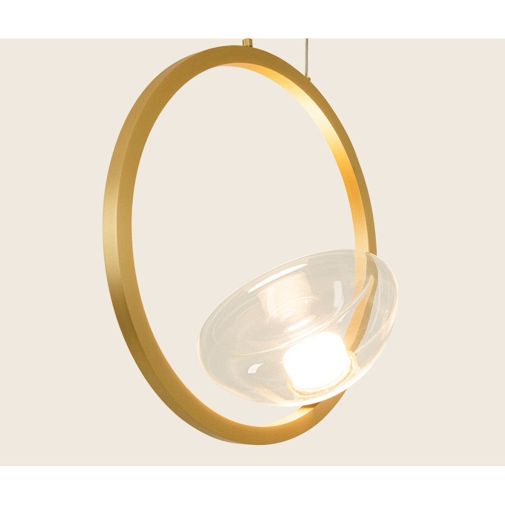 Détail rapproché du luminaire doré et de son diffuseur en verre allumé, vue inclinée.
