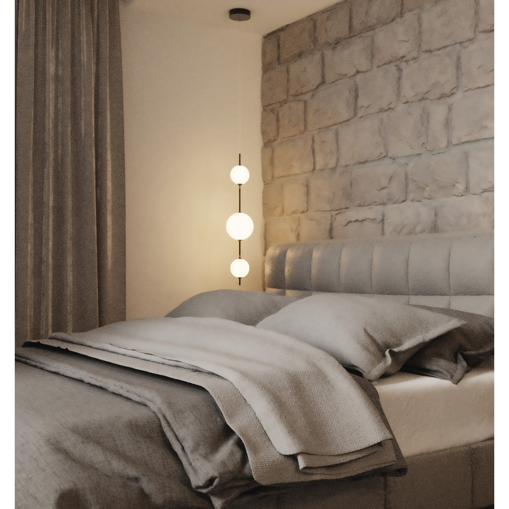 Vue rapprochée chambre, suspension allumée devant mur en pierre et lit gris.