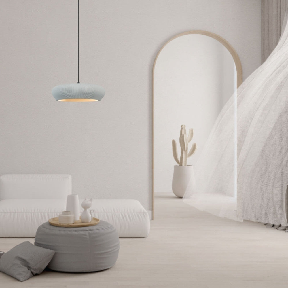 Mise en ambiance salon épuré, suspension allumée au-dessus d'un pouf gris.