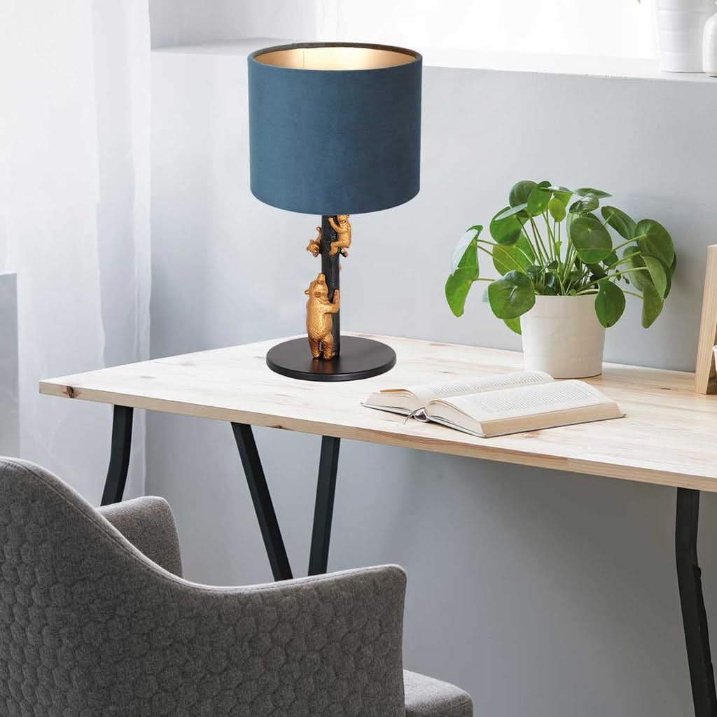 Lampe posée sur un bureau en bois, entourée d’un livre ouvert et d’une plante verte.