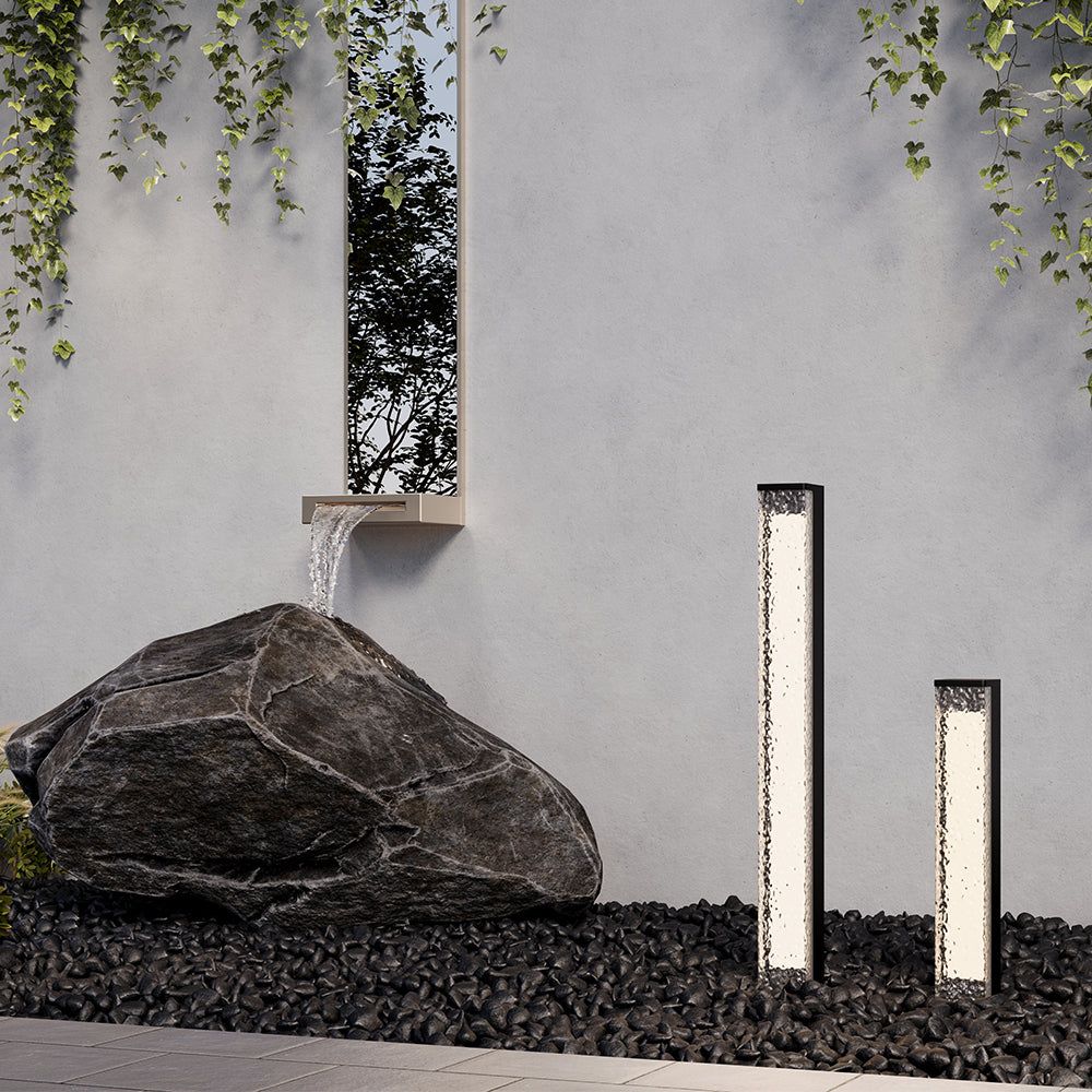 Mise en ambiance jardin avec deux bornes lumineuses près d'un rocher et d'un mur.