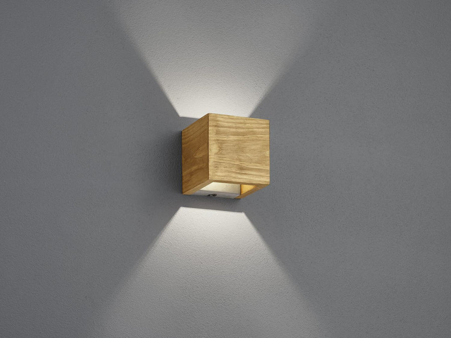 Applique murale cubique en bois clair sur mur gris, éclairage haut et bas.