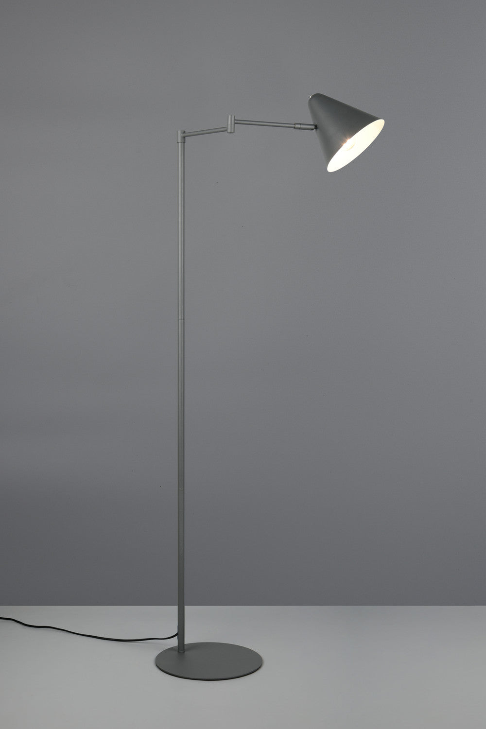 Mise en ambiance sur fond gris, lampe allumée éclairant un abat-jour conique.