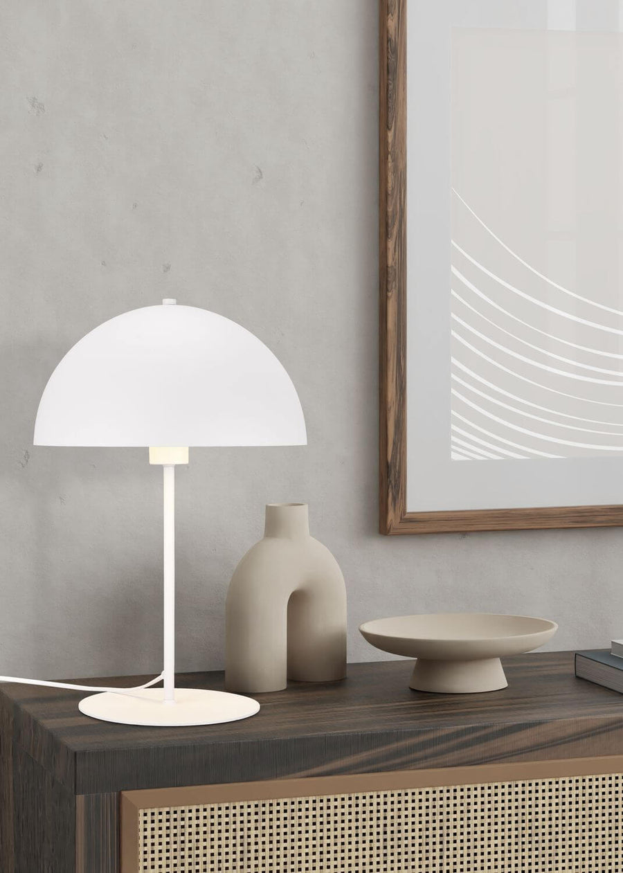 Lampe à poser blanche de face dans un intérieur, abat-jour dôme et pied fin