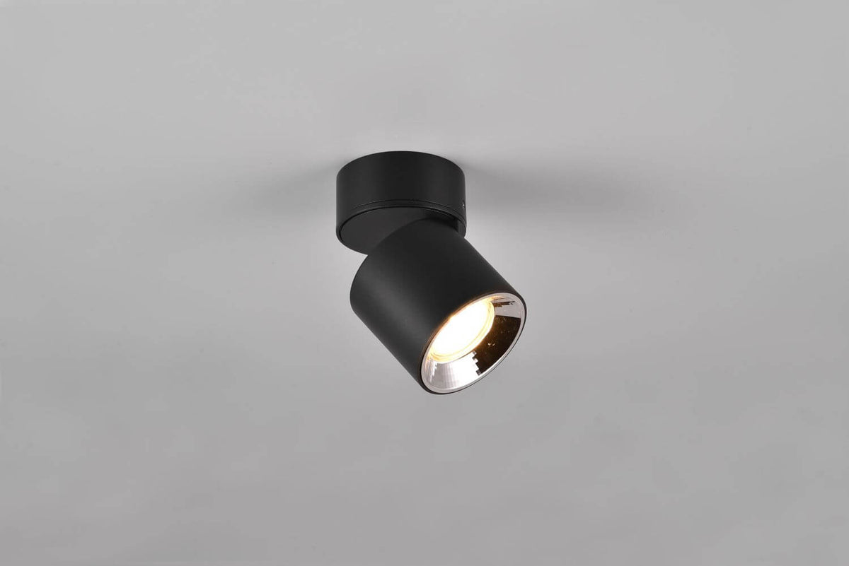 Spot plafonnier noir mat incliné éclairant une surface grise unie