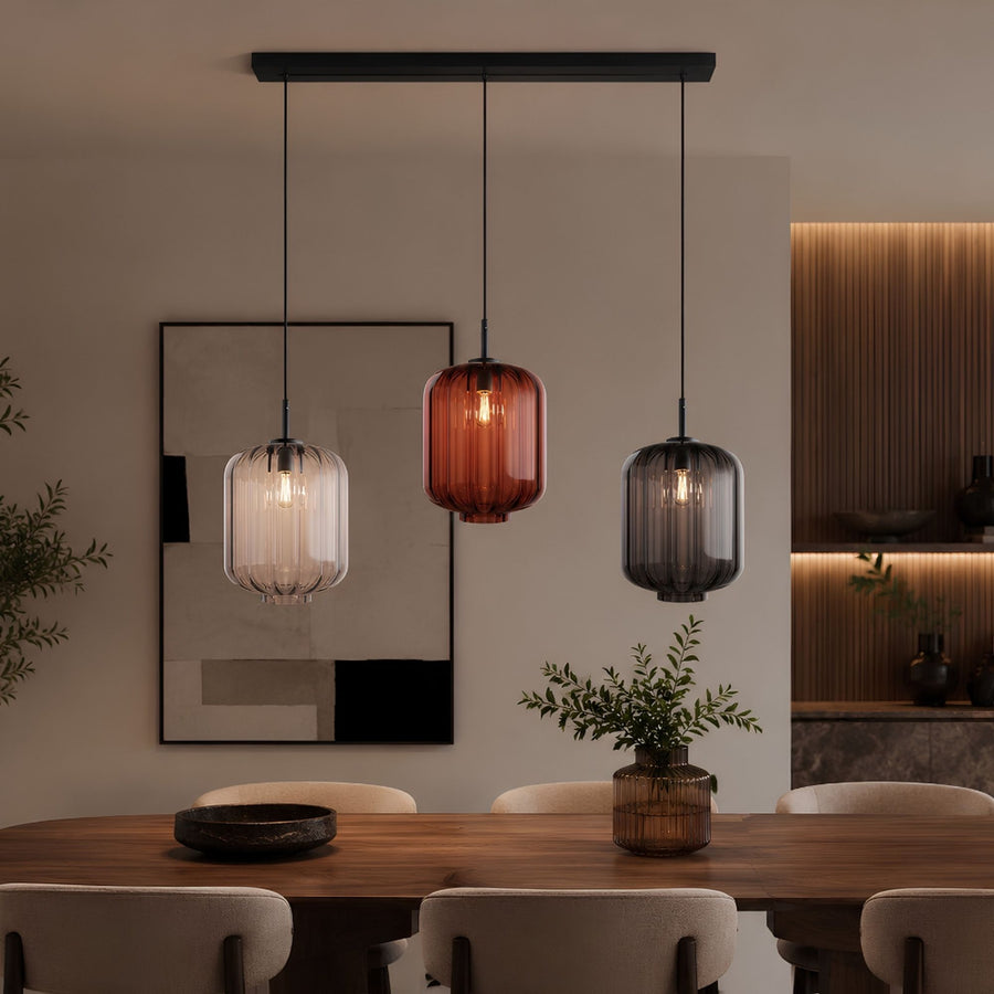 Trois suspensions en verre coloré éclairent une table à manger en bois