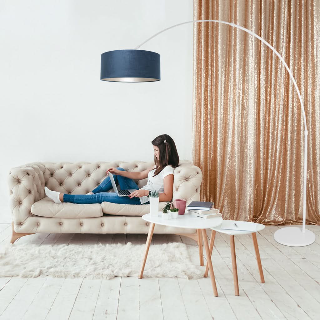Mise en ambiance dans un salon avec canapé beige, rideau doré et personne assise.